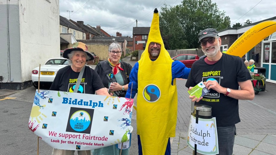 Photo of 3 members of Fairtrade with a banner and Councillor Garvey dressed in a Fairtrade banana suit