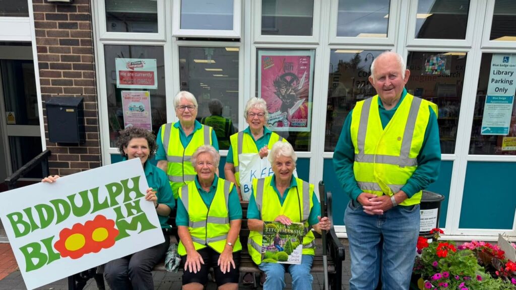 6 members of Biddulph in Bloom in yellow high viz jackets and holding a banner