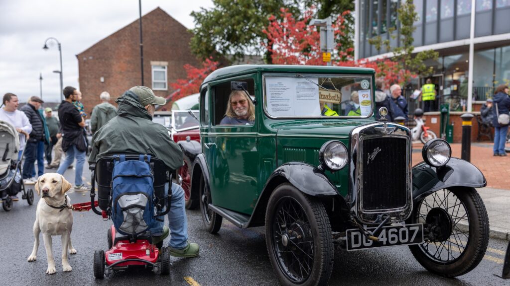 A man on a scooter with a golden labrador dog chatting to an exhibitor in front of the Town Hall